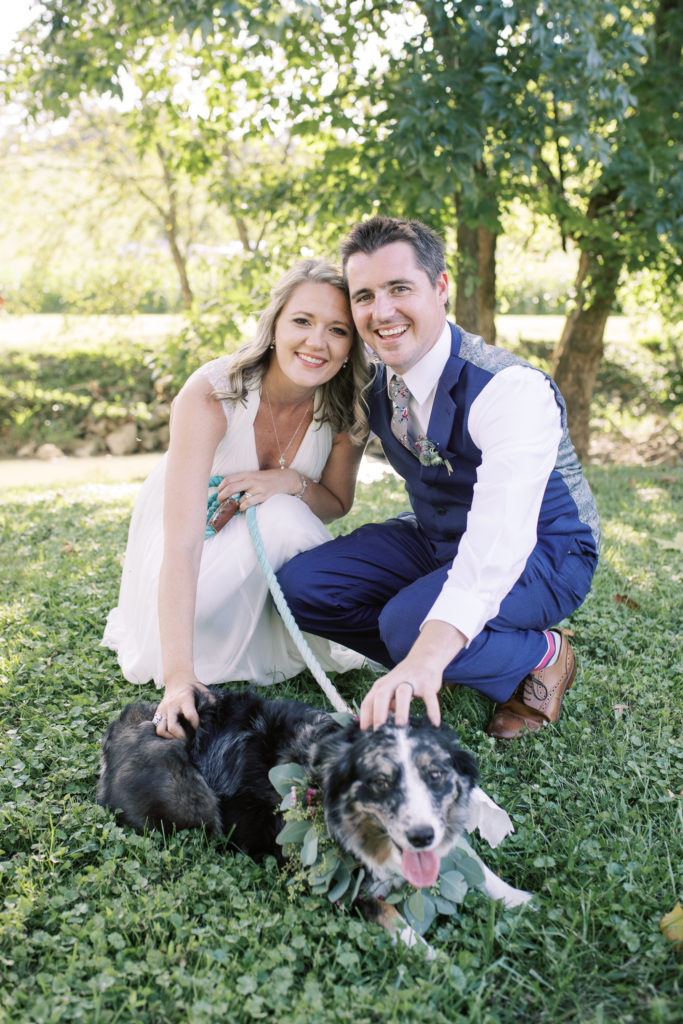 Bride and groom kneel down next to their dog and smile on their wedding day